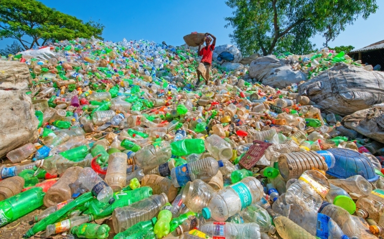 Large mound of discarded plastic; a waste picker with a basket