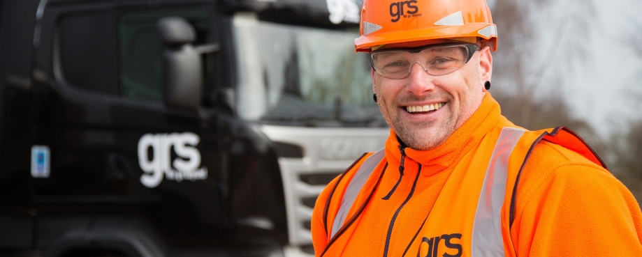 Smiling man wearing high-viz and PPE, with construction industry truck in background