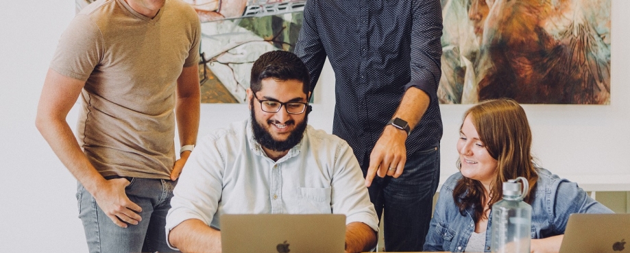 A group colleagues collaborate around a laptop. Photo credit: Jud Mackrill/ Unsplash.
