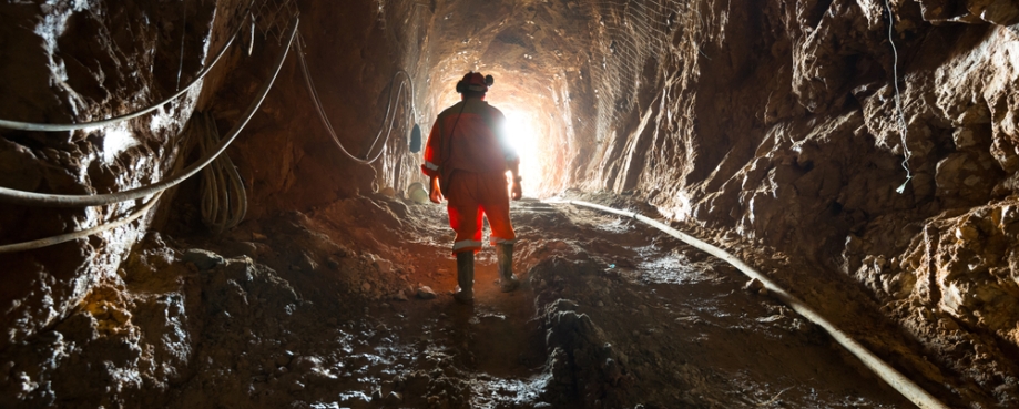 Man stands near train tracks in a mine, looking up to a lit passage way. Photo credit: Shutterstock.