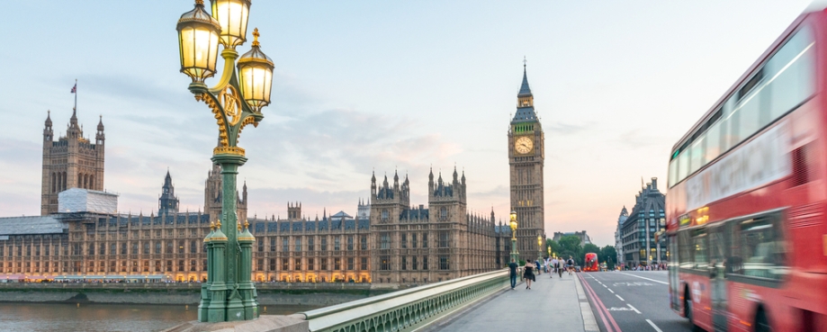 Red double decker bus speeds past UK Parliament, London. Photo credit: Shutterstock.