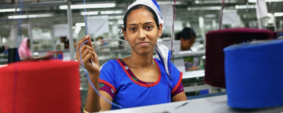A woman garment worker looks up to the camera as she works in knitting section. Photo credit: Shutterstock.