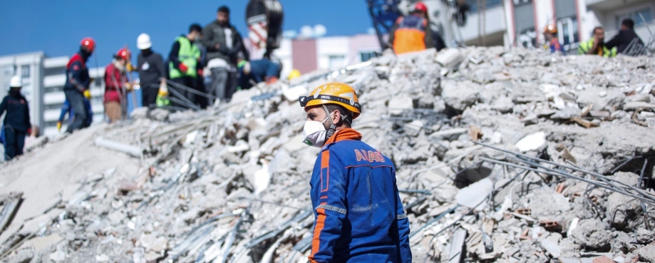 A man wearing a mask and helmet stands amid the rumble following an earthquake. Photo credit: murat photographer