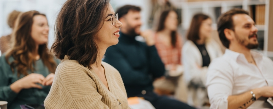 Smiling woman participating in a professional workshop with colleagues in a modern office setting, conveying engagement and teamwork. Photo credit: Shutterstock.