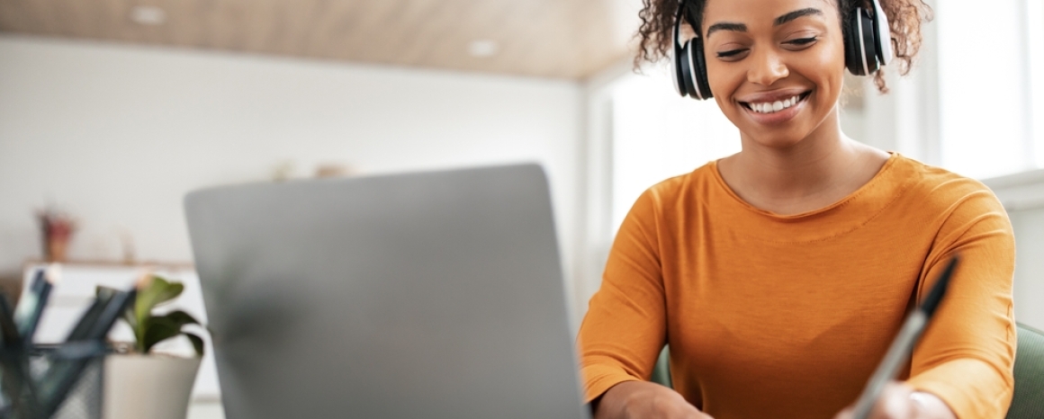 Smiling woman wearing headphones, studying with laptop and notebook