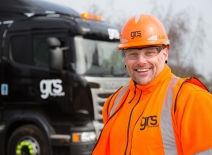 Smiling man wearing high-viz and PPE, with construction industry truck in background