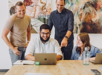 A group colleagues collaborate around a laptop. Photo credit: Jud Mackrill/ Unsplash.