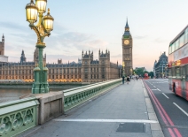 Red double decker bus speeds past UK Parliament, London. Photo credit: Shutterstock.