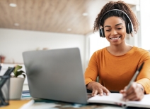 Smiling woman wearing headphones, studying with laptop and notebook