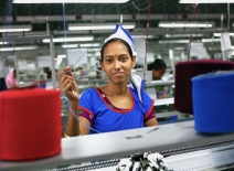 A woman garment worker looks up to the camera as she works in knitting section. Photo credit: Shutterstock.