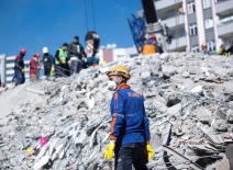 A man wearing a mask and helmet stands amid the rumble following an earthquake. Photo credit: murat photographer