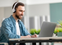 Bearded man wearing headphones, smiling at laptop
