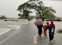 Two women and two children walk along a flooded road in Bangladesh. Photo credit: Shutterstock.
