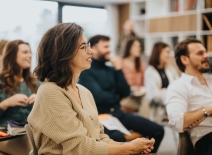 Smiling woman participating in a professional workshop with colleagues in a modern office setting, conveying engagement and teamwork. Photo credit: Shutterstock.