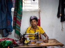 Young boy sits at a sewing machine in a yellow t-shirt. (Photo credit: Shutterstock).